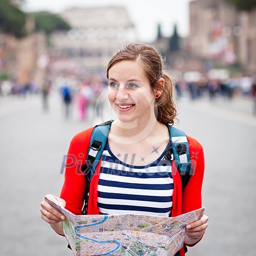 Pretty young female tourist holding a map while walking along the Via del Fori Imperiali avenue in Rome, Italy (with Colosseum in the background)