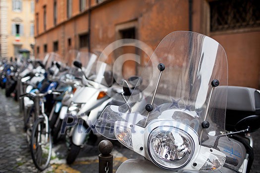 Row of motorbikes and scooters parked in one of the ancient streets of Rome Row of motorbikes and scooters parked in one of the ancient streets of Rome