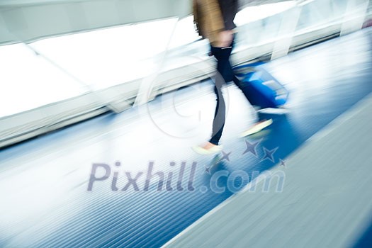 Airport rush: people with their suitcases walking along a corridor (motion blurred image; color toned image)