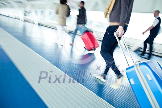 Airport rush: people with their suitcases walking along a corridor (motion blurred image; color toned image)