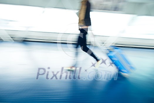 Airport rush: people with their suitcases walking along a corridor (motion blurred image; color toned image)