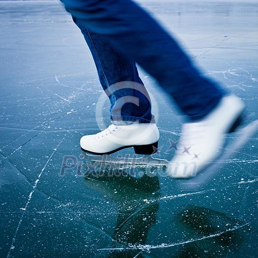 Young woman ice skating outdoors on a pond on a freezing winter day - detail of the legs
