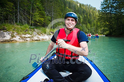 white water rafting - young man in a raft boat,  paddling, smiling