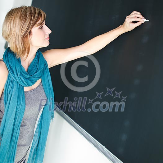 pretty young college student/young teacher writing on the chalkboard/blackboard during a math class (color toned image; shallow DOF)