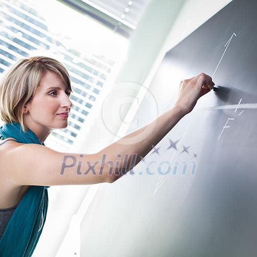 pretty young college student/young teacher writing on the chalkboard/blackboard during a math class (color toned image; shallow DOF)