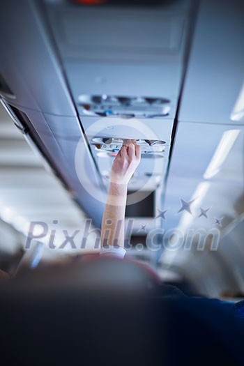 Passenger adjusting air conditioning above his seat while on board of an aircraft