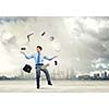 Young businessman juggling with business items against urban scene