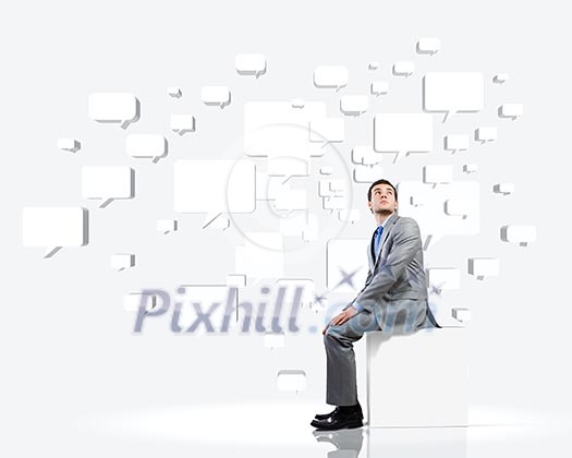 Young handsome businessman sitting on white cube