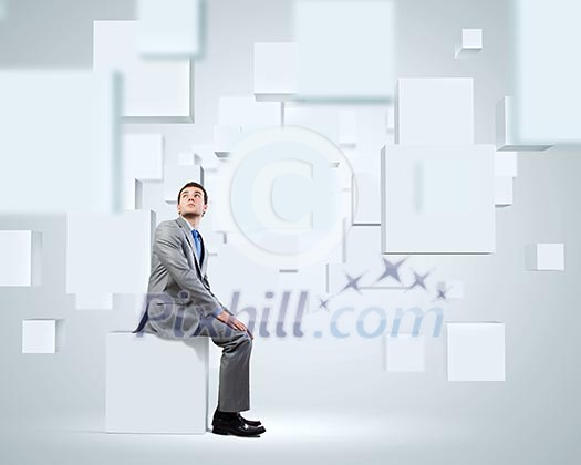 Young handsome businessman sitting on white cube