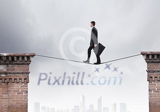 Conceptual image of businessman walking on rope above gap Conceptual image of businessman walking on rope above gap