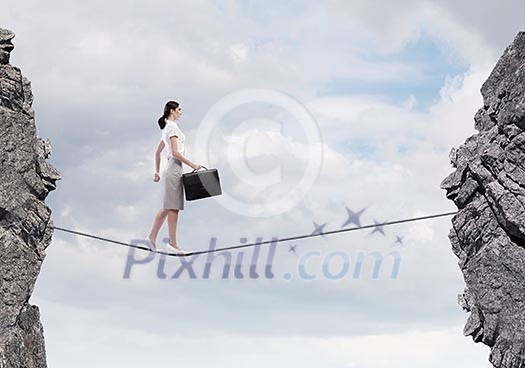 Young confident businesswoman walking on rope above gap Young confident businesswoman walking on rope above gap