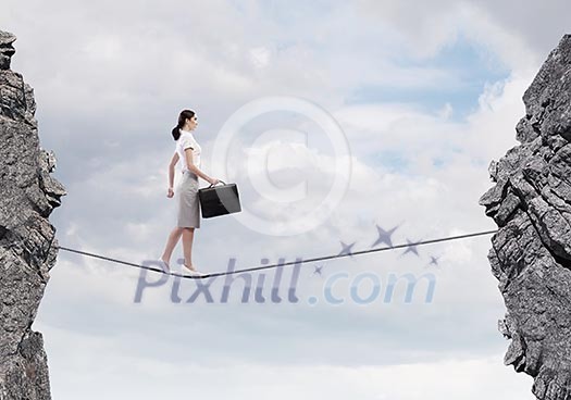 Young confident businesswoman walking on rope above gap