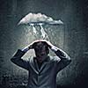 Businessman sitting under rain protecting head with arms