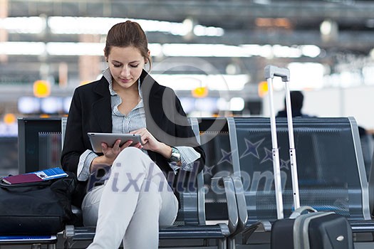 Young female passenger at the airport, using her tablet computer while waiting for her flight Young female passenger at the airport, using her tablet computer while waiting for her flight