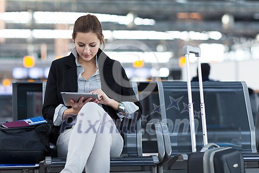 Young female passenger at the airport, using her tablet computer while waiting for her flight