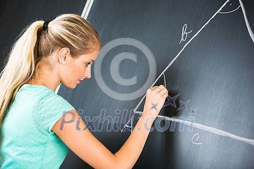 Pretty young elementary school/college teacher writing on the chalkboard/blackboa rd during a math class (color toned image; shallow DOF)