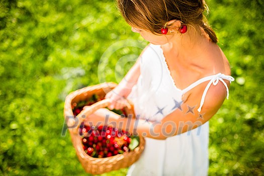 Beautiful young woman holding a basket filled with freshly picked cherries