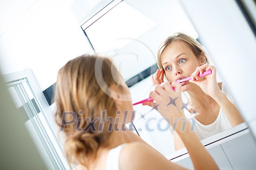 Pretty female brushing her teeth in front of mirror in the morning, making silly faces, checking her skin