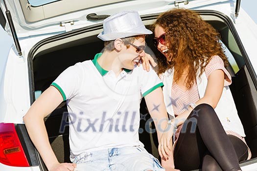 Young happy couple sitting in car trunk outdoor Young happy couple sitting in car trunk outdoor