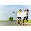 Two pretty young girls standing aside road with blank white banner