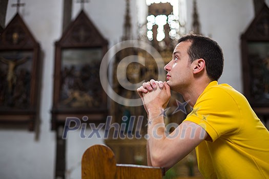 Handsome young man praying in a church Handsome young man praying in a church