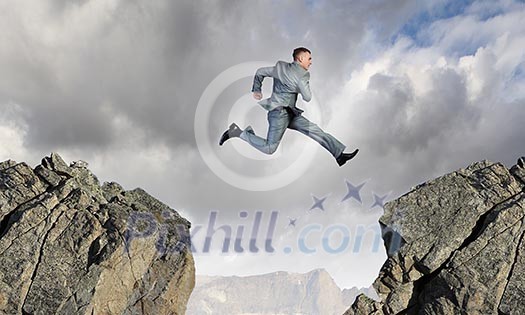 Young businessman jumping over mountain gap. Risking in business Young businessman jumping over mountain gap. Risking in business