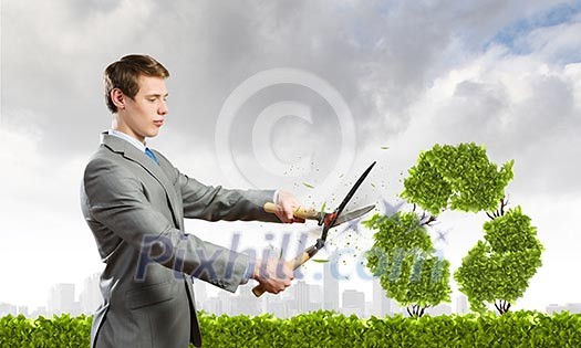 Young businessman cutting bush in shape of recycle symbol Young businessman cutting bush in shape of recycle symbol