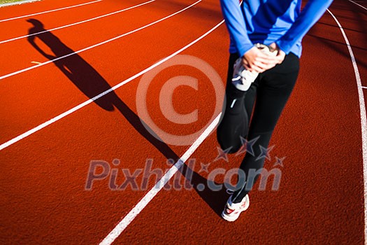 Young woman stretching before her run casts a shadow on the track