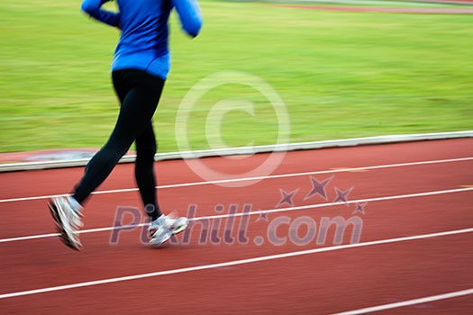 Young woman running at a track and field stadium (motion blurred image)