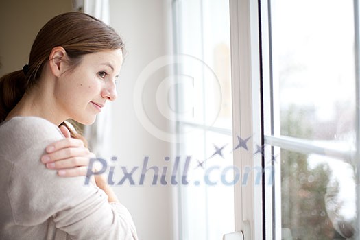 Woman lookong from a window of her house on a cold and snowy winter day