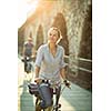 Pretty, young woman riding a bicycle in a city with her boyfriend (color toned image; shallow DOF)