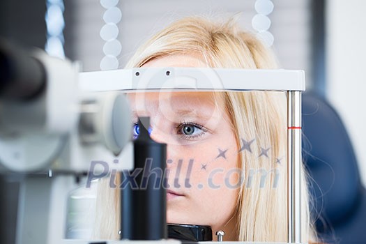 Optometry concept - pretty, young female patient having her eyes examined by an eye doctor (color toned image; shallow DOF)