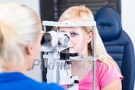 Optometry concept - pretty, young female patient having her eyes examined by an eye doctor (color toned image; shallow DOF)