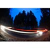 Cars going fast through a curve on a forest road at dusk, on a rainy day - i.e. Potentially dangerous driving conditions