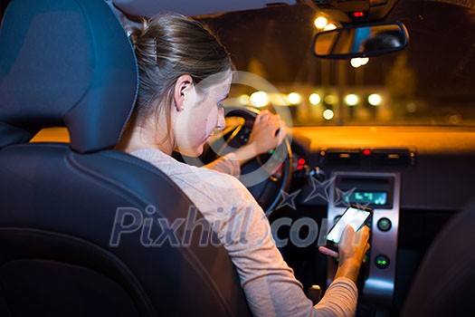 Pretty young woman using her smart phone while driving her car at night
