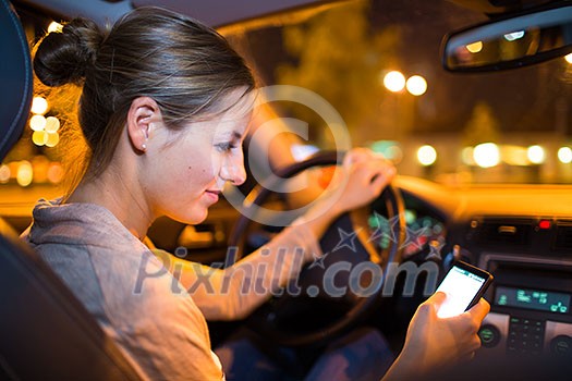 Pretty young woman using her smart phone while driving her car at night