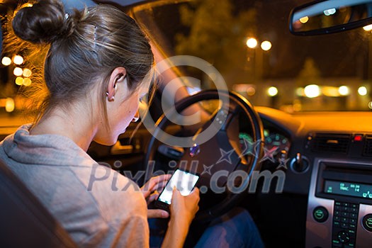 Pretty young woman using her smart phone while driving her car at night