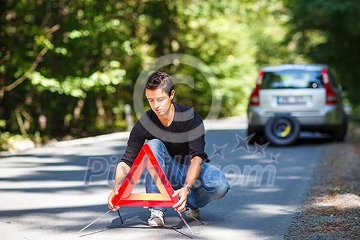 Handsome young man with his car broken down by the roadside, setting the safety triangle