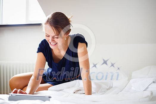 Elegant, smart, young woman using her tablet computer in bed (shallow DOF; color toned image)