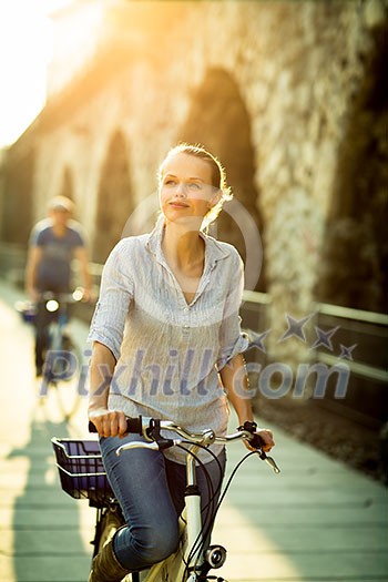 Pretty, young woman riding a bicycle in a city with her boyfriend (color toned image; shallow DOF)