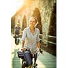 Pretty, young woman riding a bicycle in a city with her boyfriend (color toned image; shallow DOF)