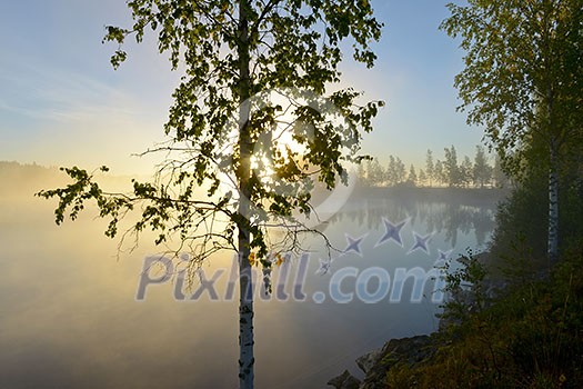 Sunrise over a calm lake on a misty morning