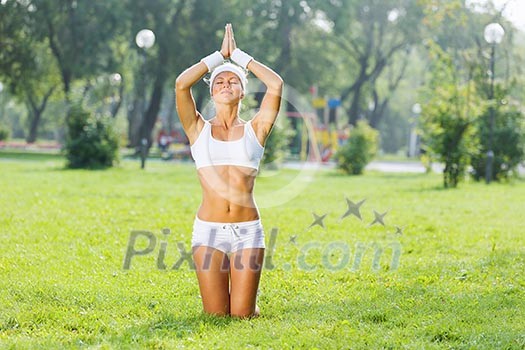 Young woman in white sitting on grass and practicing yoga