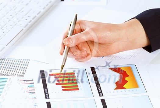 Close up of male hand holding pen and pointing at graphs Close up of male hand holding pen and pointing at graphs