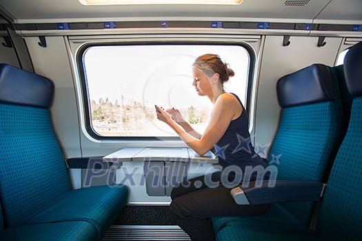Young woman traveling by train, using her smartphone while sitting on board, alone