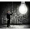 Businessman switching on light bulb with business sketches at background