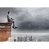 Businessman sitting on top of building and fishing with rod