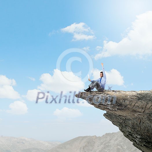 Young businessman sitting on edge of rock mountain and using tablet pc