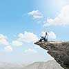 Young businessman sitting on edge of rock mountain and using tablet pc