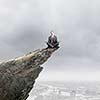 Young businessman sitting lotus pose on edge of rock mountain